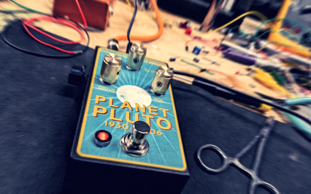 Somewhat grainy angle shot of a guitar effect pedal on a workbench, showing radiance emanating from a poorly drawn (former) planet Pluto